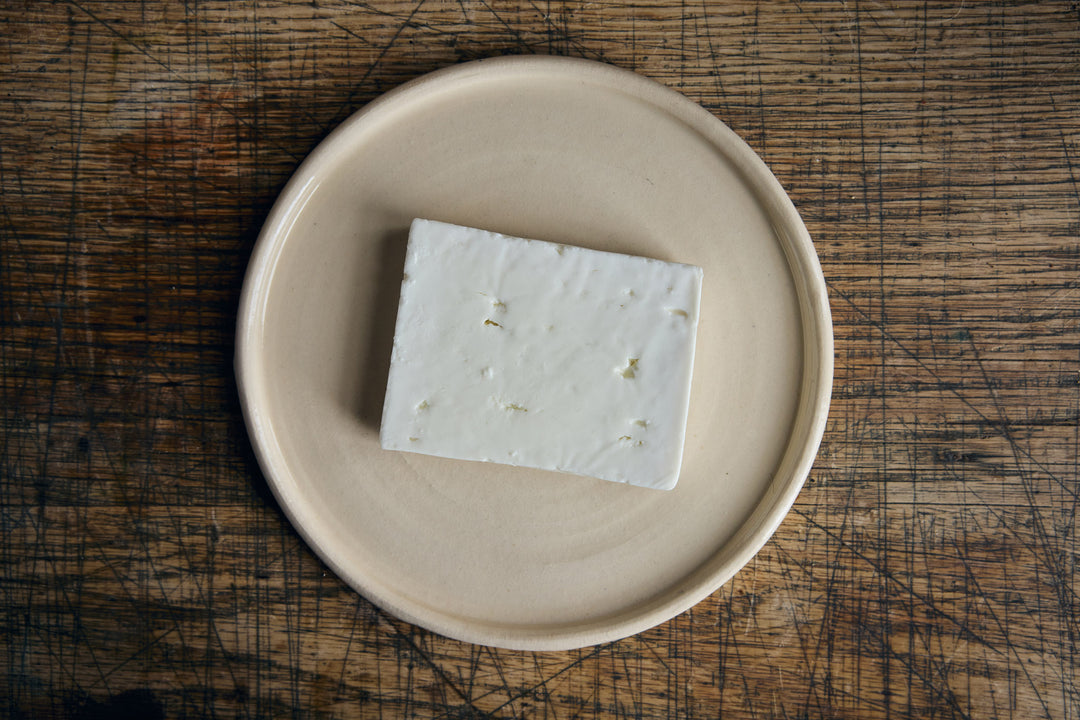 Block of white cheese on a beige plate on a wooden surface