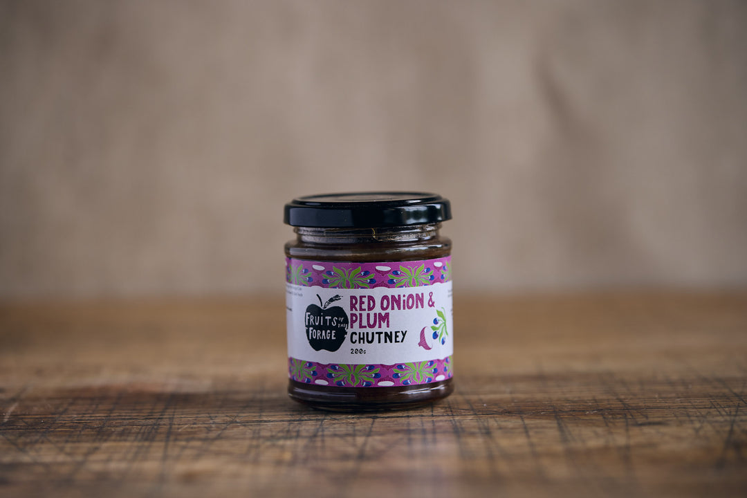Jar of red onion and plum chutney on a wooden surface with a brown background