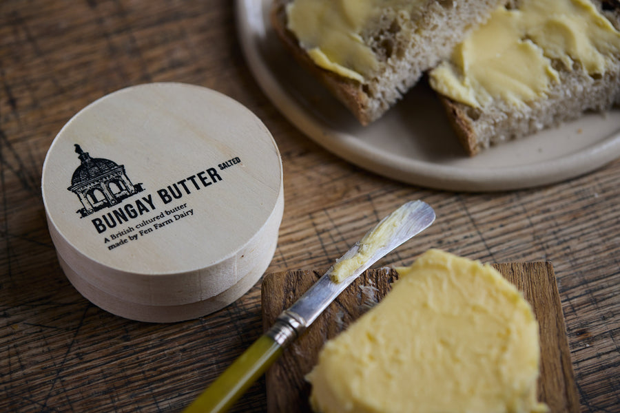 Bungay Butter jar with a knife spreading butter on bread, on a wooden surface.