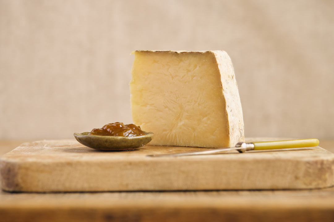 Block of cheese with a spoonful of jam on a wooden board against a beige background